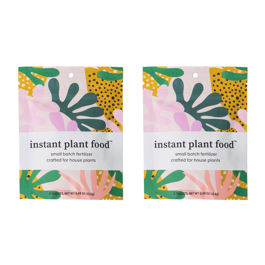Two Instant Plant Food sachet packets showcasing vibrant pink, yellow, and teal botanical leaf pattern design, small batch fertilizer tablets crafted for thriving indoor houseplants and plant parent care.