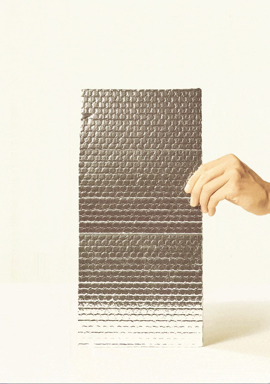 Hand holding a piece of reflective, bubble-textured thermal insulation material used for winter plant shipping.