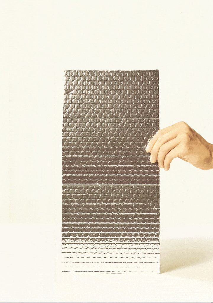 Hand holding a piece of reflective, bubble-textured thermal insulation material used for winter plant shipping.