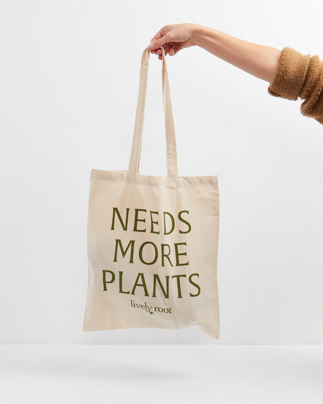 Lively Root canvas tote bag with "Needs More Plants" bold green text and natural cotton handles, reusable and durable eco-friendly shopping tote designed for plant parents and sustainable home gardening.